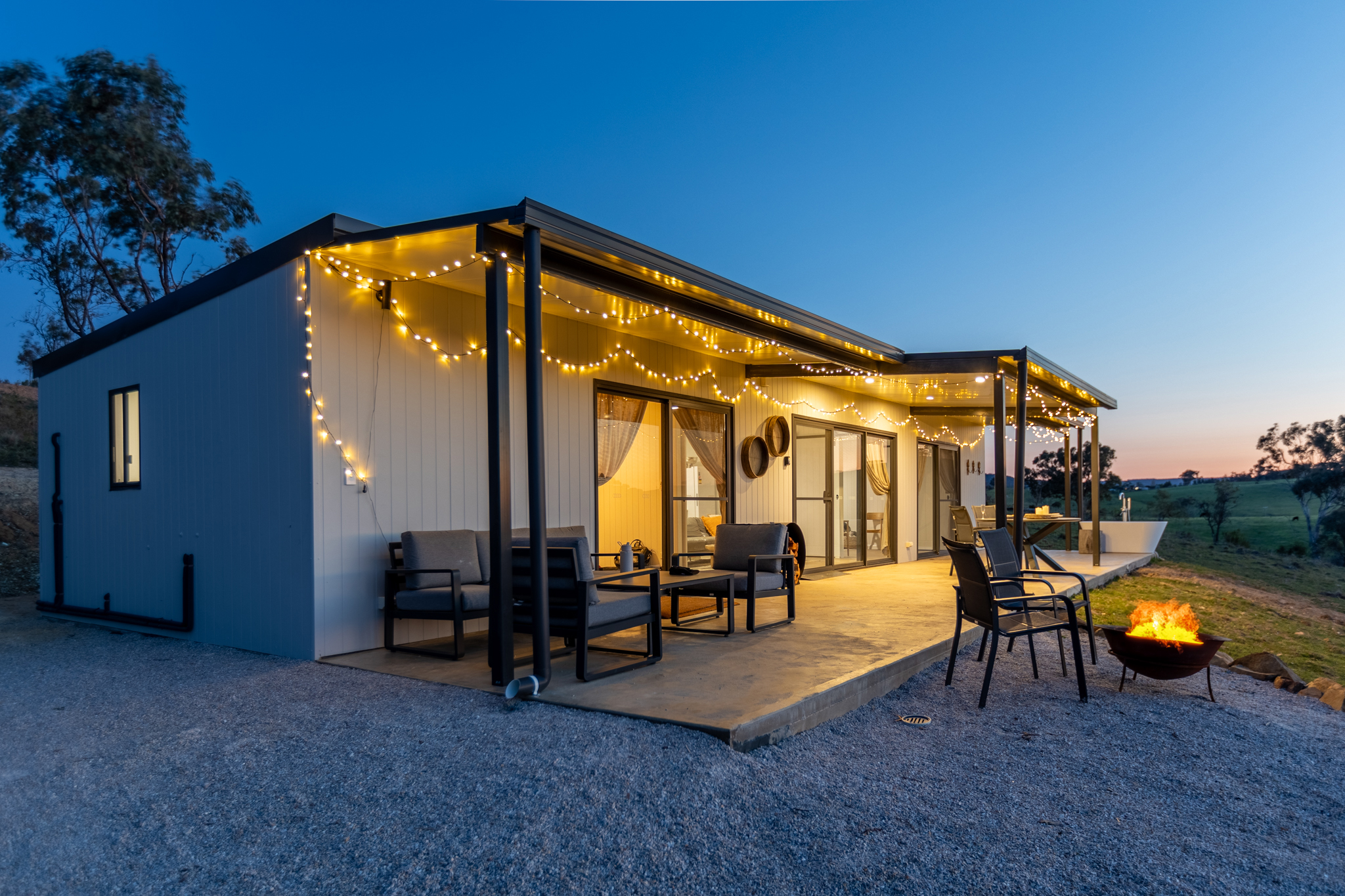 Cabin with fire pit and fairy lights at dusk